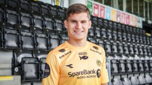 Nino Zugelj smilende i gul hjemmedrakt på tribunen på Aspmyra.