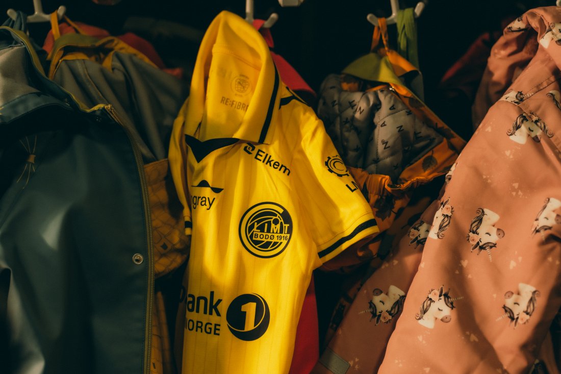 En bitteliten Bodø/Glimt-drakt henger på en knaggrekke i en barnehagegarderobe