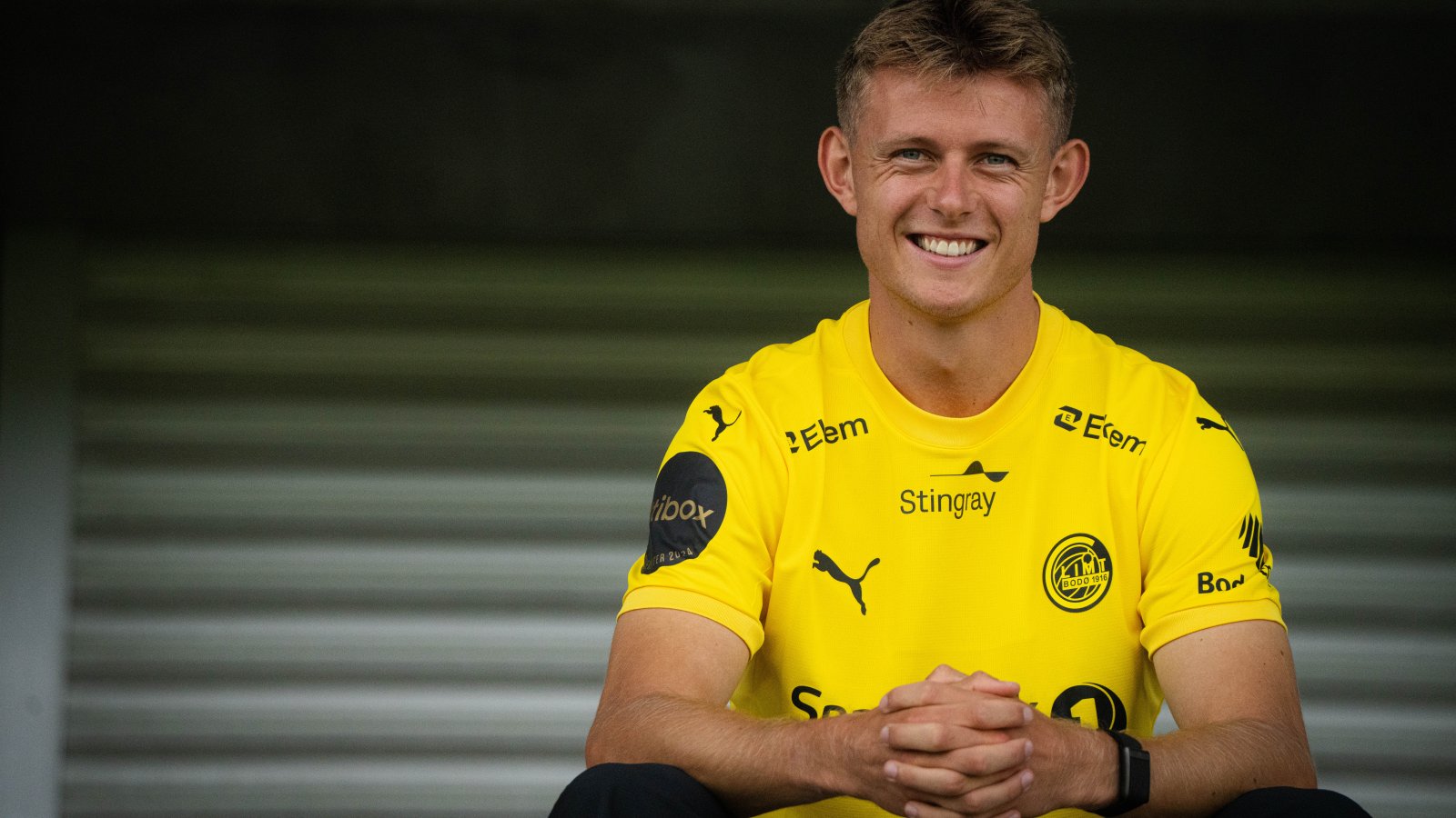 En smilende Mathias Jørgensen sitter på Aspmyra med foldede hender. 