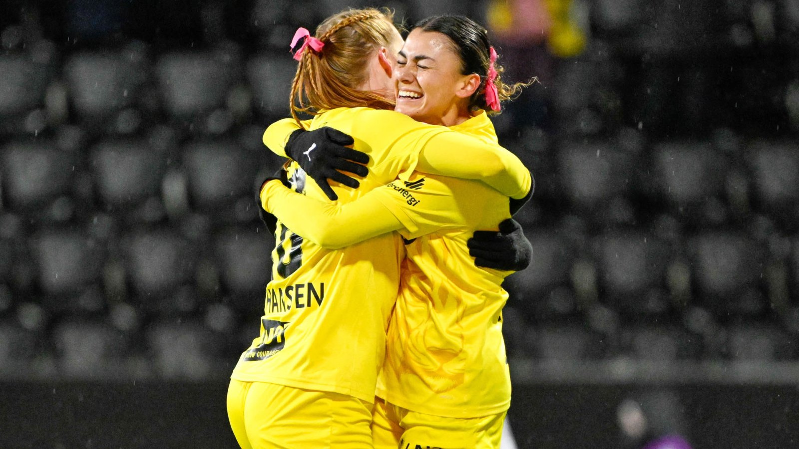 Claudia Cagnina og Anna Johansen klemmer hverandre og smiler i gule drakter med rosa sløyfe i håret under kampen mot viking på Aspmyra høsten 2024.